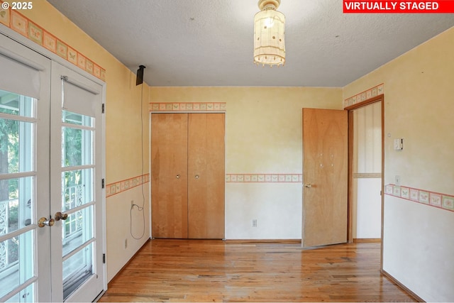 unfurnished bedroom featuring french doors, a textured ceiling, a closet, and wood finished floors