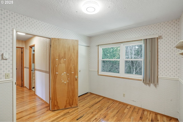 unfurnished bedroom featuring a textured ceiling, wallpapered walls, and wood finished floors