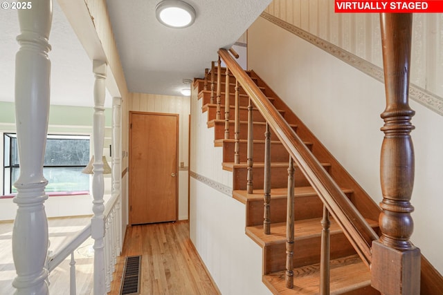 staircase featuring visible vents, a textured ceiling, decorative columns, and wood finished floors