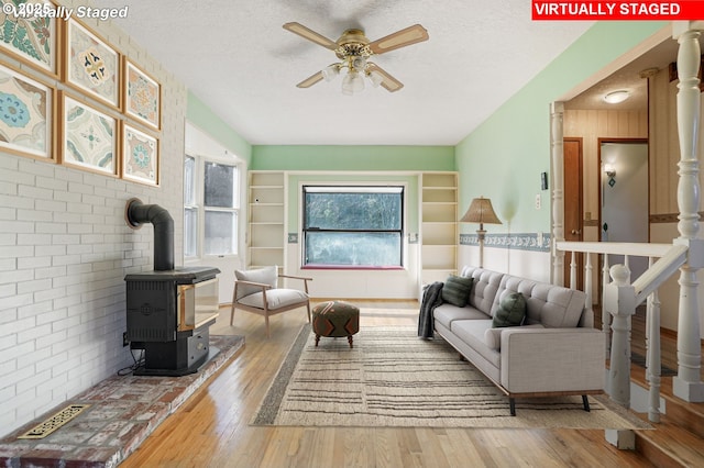 living area featuring a ceiling fan, a textured ceiling, wood finished floors, and a wood stove