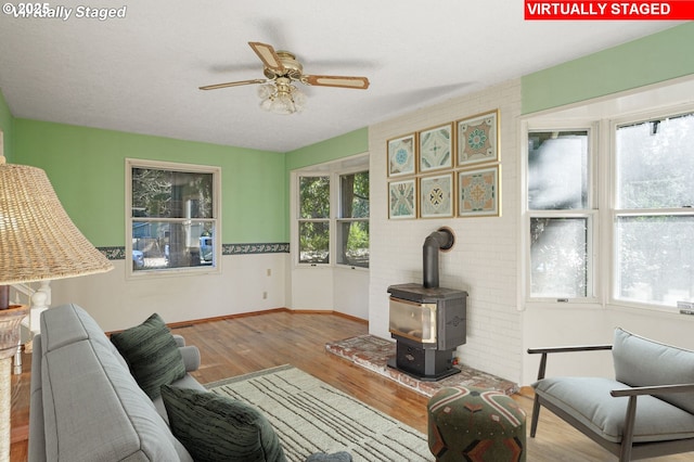 living area featuring a ceiling fan, a wood stove, wood finished floors, and baseboards