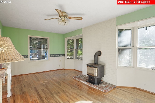 unfurnished living room featuring a ceiling fan, a wood stove, baseboards, and wood finished floors