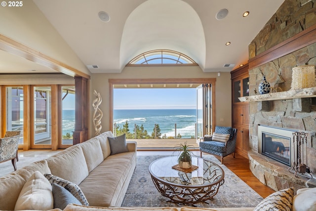 280 Fall Creek Dr, Oceanside, OR 97134 - living area featuring vaulted ceiling, a stone fireplace, a water view, wood finished floors, and recessed lighting