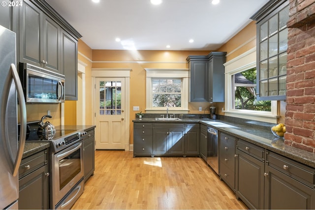 kitchen featuring dark stone counters, appliances with stainless steel finishes, light hardwood / wood-style flooring, and sink