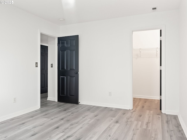 unfurnished bedroom with a walk in closet, light hardwood / wood-style floors, and a closet