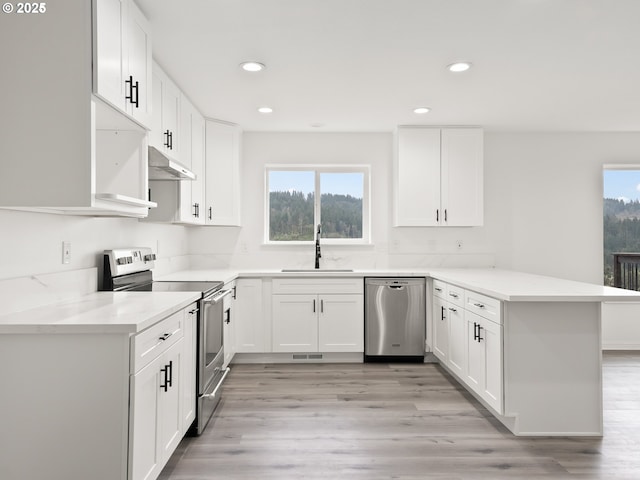 kitchen with sink, light wood-type flooring, kitchen peninsula, stainless steel appliances, and white cabinets