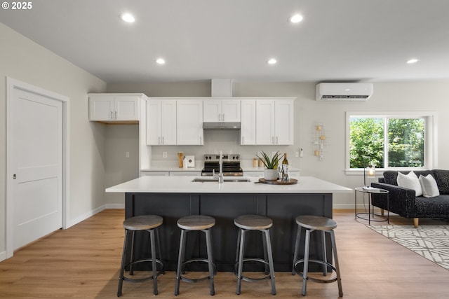 4221 Hudson Ave, Salem, OR 97301 - kitchen with a wall mounted air conditioner, white cabinetry, an island with sink, light wood finished floors, and recessed lighting