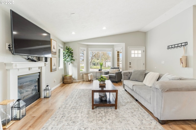 living area featuring baseboards, recessed lighting, wood finished floors, vaulted ceiling, and a glass covered fireplace