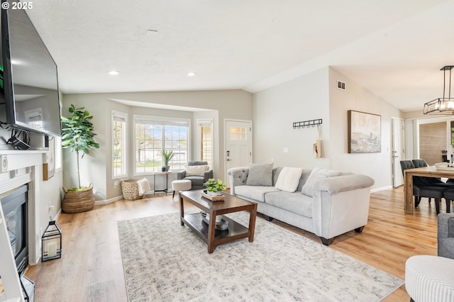 living room featuring visible vents, baseboards, wood finished floors, a glass covered fireplace, and lofted ceiling