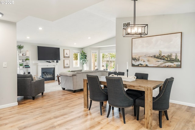 dining area with light wood-style floors, an inviting chandelier, a glass covered fireplace, recessed lighting, and baseboards