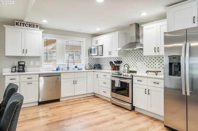 kitchen with wall chimney exhaust hood, white cabinets, appliances with stainless steel finishes, light countertops, and a sink