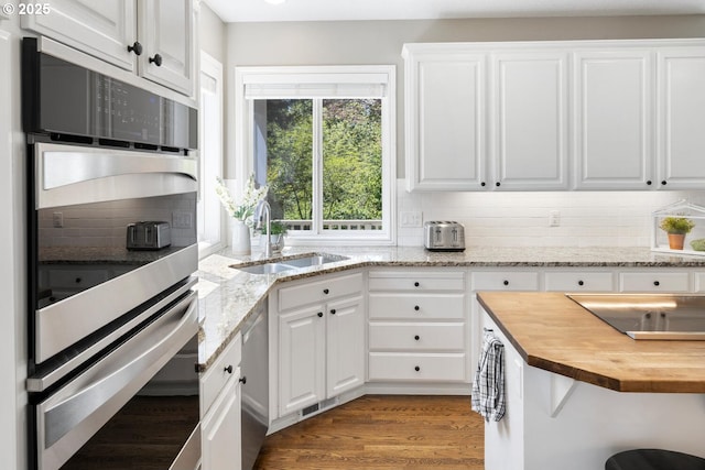 kitchen with wooden counters, a sink, tasteful backsplash, and white cabinets