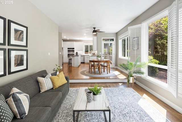 living area featuring light wood-style flooring, baseboards, and a ceiling fan