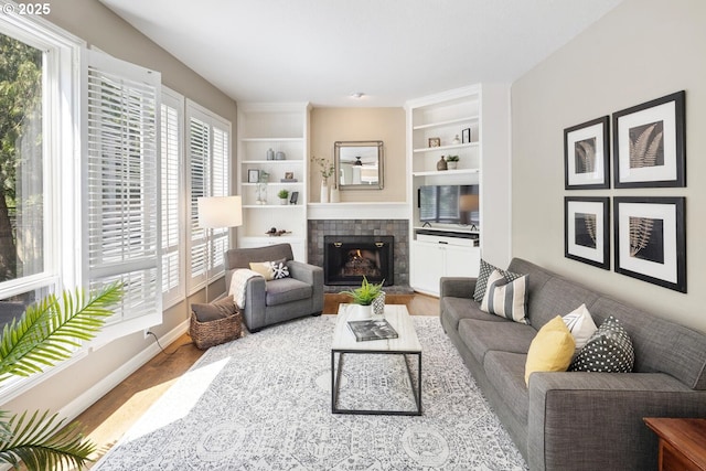 living area featuring wood finished floors, a fireplace, built in shelves, and baseboards