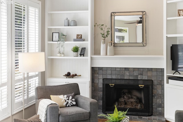 sitting room with built in shelves, a fireplace, and a ceiling fan