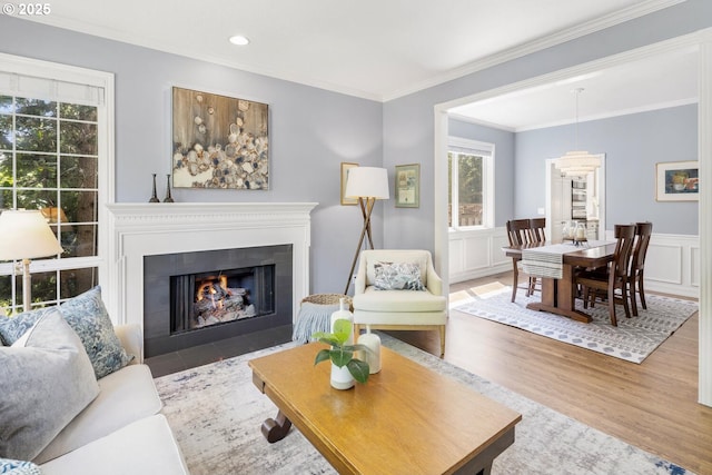 living room with crown molding, wood finished floors, recessed lighting, a wainscoted wall, and a fireplace with flush hearth