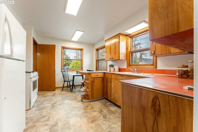 kitchen featuring brown cabinets, light countertops, a sink, white appliances, and a peninsula