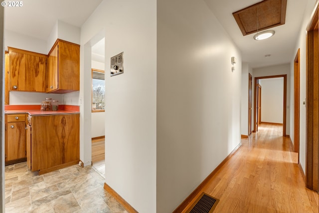 hall with light wood-style floors, baseboards, and visible vents