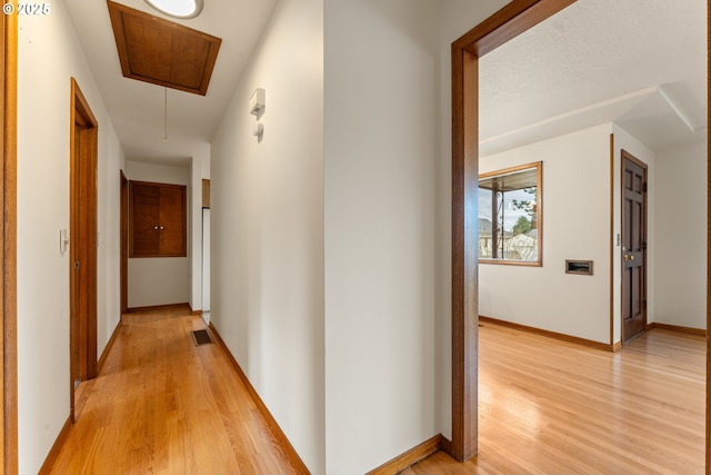 hallway featuring visible vents, light wood finished floors, attic access, and baseboards