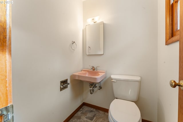 bathroom with toilet, stone finish flooring, baseboards, and a sink