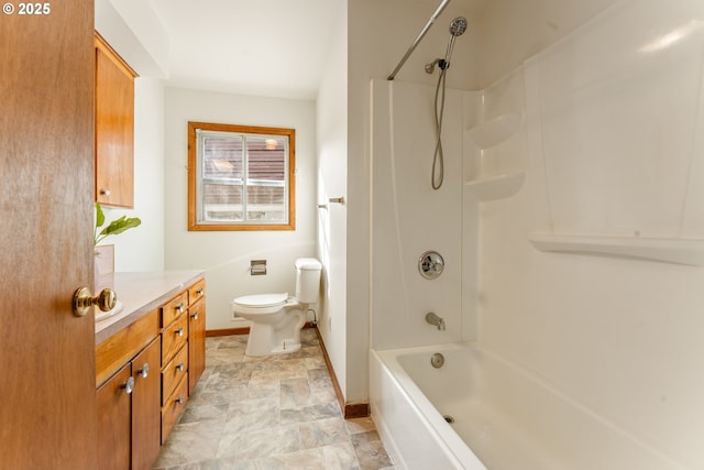 bathroom featuring shower / washtub combination, toilet, stone finish floor, vanity, and baseboards