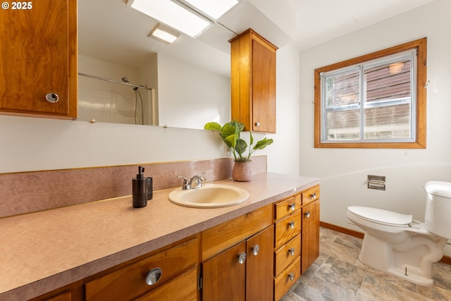 full bath featuring toilet, vanity, baseboards, stone finish floor, and walk in shower