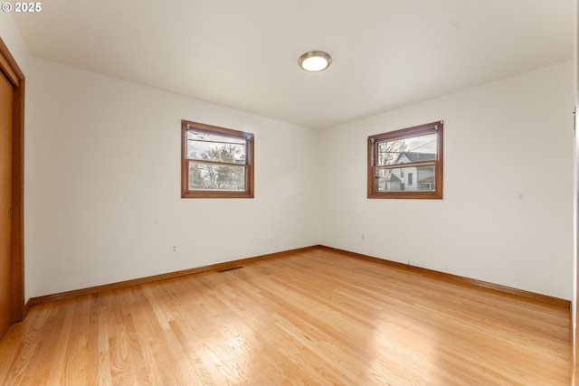 unfurnished room featuring baseboards, light wood-type flooring, visible vents, and a healthy amount of sunlight