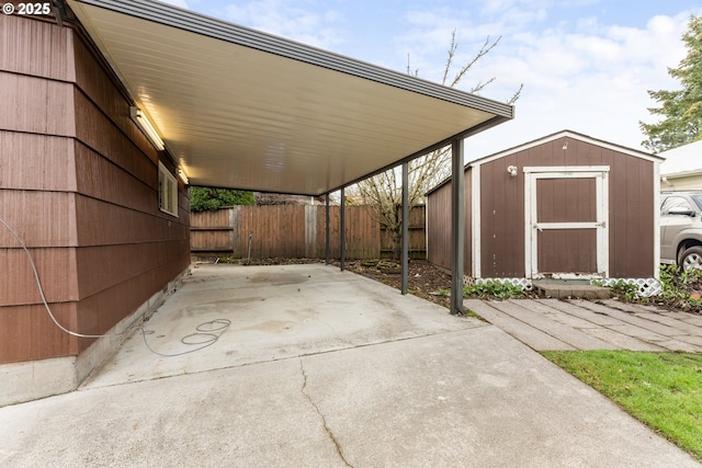 view of patio / terrace with a storage unit, concrete driveway, fence, an attached carport, and an outdoor structure