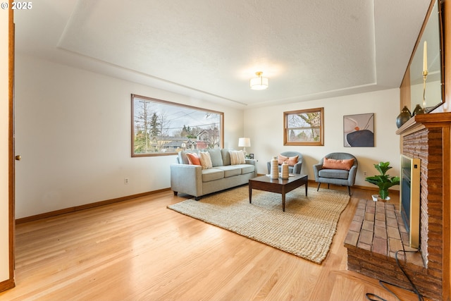 living room with a brick fireplace, plenty of natural light, baseboards, and wood finished floors