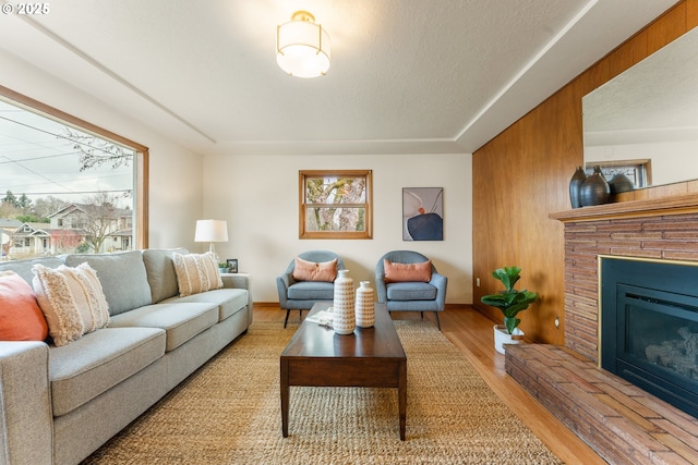 living area featuring a textured ceiling, wood finished floors, a glass covered fireplace, and baseboards