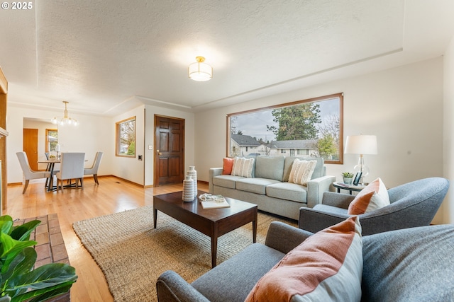 living room featuring light wood-style floors, baseboards, a textured ceiling, and an inviting chandelier