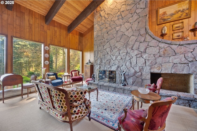 carpeted living area featuring wooden walls, a healthy amount of sunlight, beam ceiling, a stone fireplace, and wooden ceiling