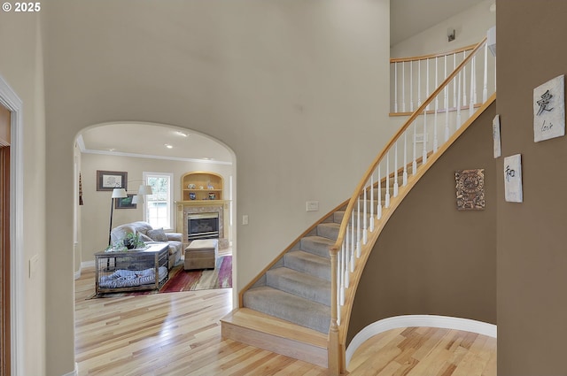 stairway featuring a towering ceiling, wood-type flooring, and ornamental molding