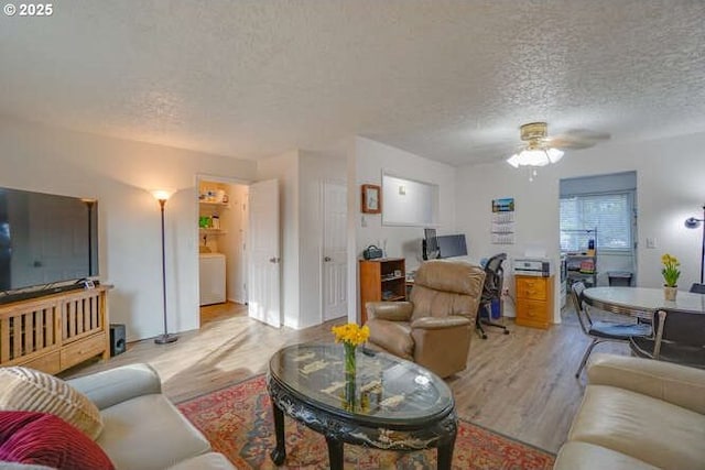 living area featuring washer / clothes dryer, a ceiling fan, light wood finished floors, and a textured ceiling