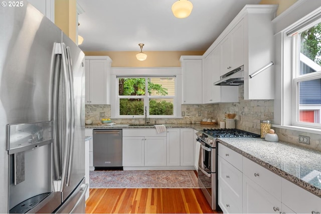 kitchen featuring appliances with stainless steel finishes, under cabinet range hood, a sink, white cabinetry, and decorative backsplash