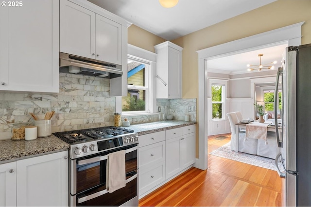 kitchen featuring stainless steel appliances, under cabinet range hood, light wood-style floors, white cabinets, and a chandelier