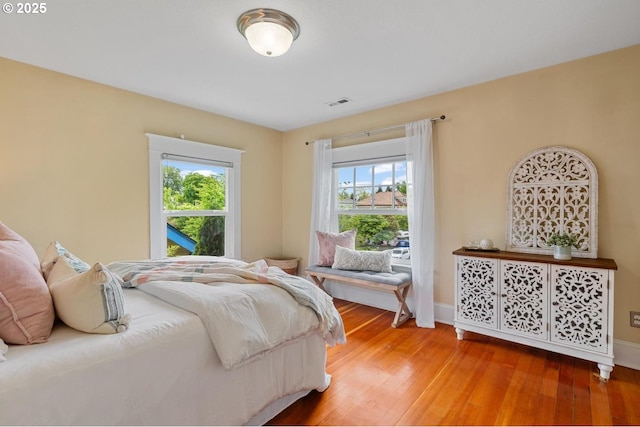 bedroom with multiple windows, wood finished floors, and baseboards