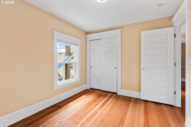 unfurnished bedroom featuring light wood-type flooring, baseboards, and a closet
