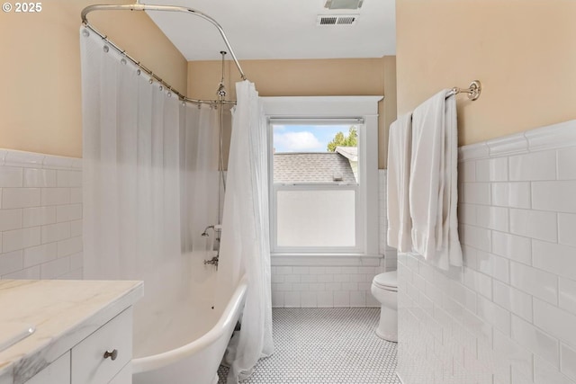 bathroom featuring tile walls, a wainscoted wall, tile patterned floors, toilet, and vanity