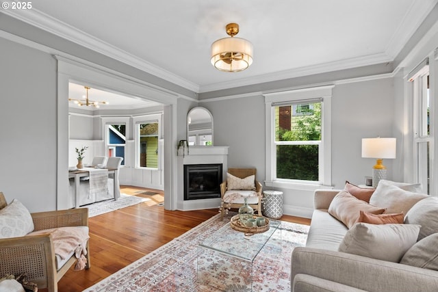 living room featuring a chandelier, wood finished floors, ornamental molding, a glass covered fireplace, and baseboards