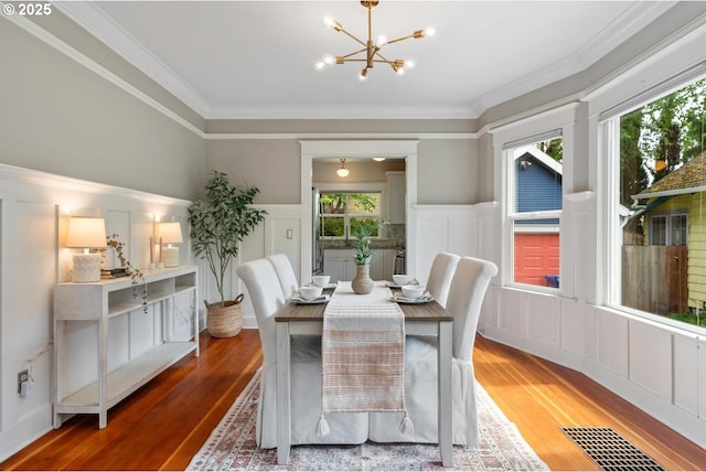 dining room with a decorative wall, wood finished floors, a chandelier, crown molding, and wainscoting