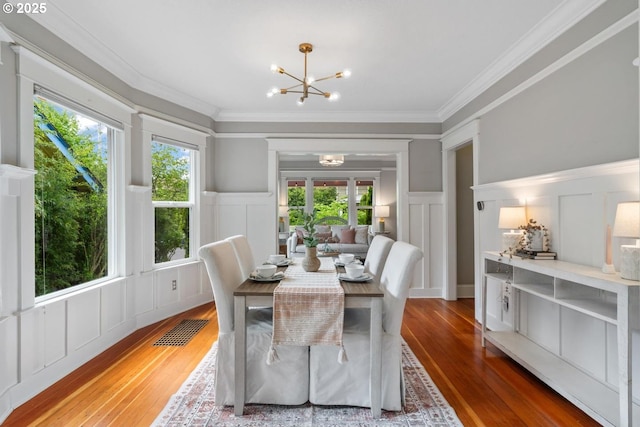 dining space featuring a decorative wall, hardwood / wood-style flooring, a chandelier, crown molding, and plenty of natural light