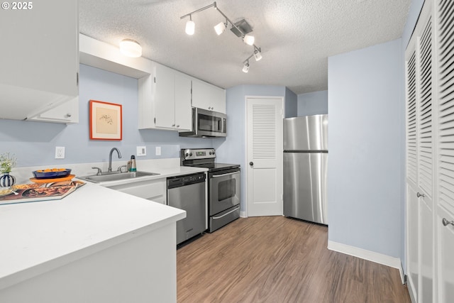 kitchen featuring a textured ceiling, appliances with stainless steel finishes, wood finished floors, a sink, and light countertops