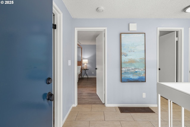 hallway featuring baseboards, a textured ceiling, and light tile patterned floors