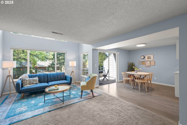 living area featuring baseboards, a textured ceiling, visible vents, and wood finished floors