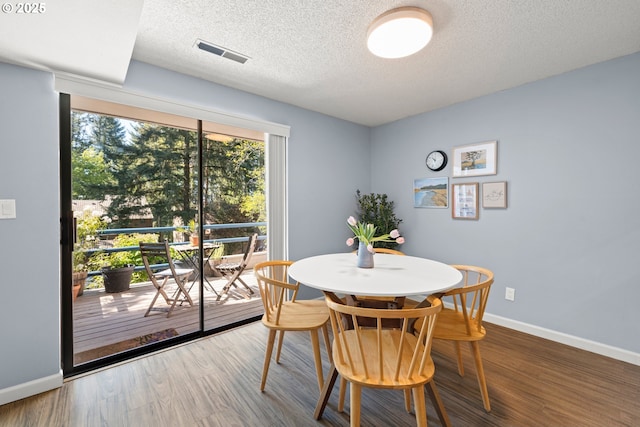 dining room with baseboards, a textured ceiling, wood finished floors, and visible vents