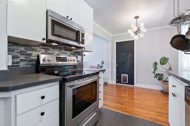 kitchen with decorative backsplash, ornamental molding, dark countertops, a chandelier, and stainless steel appliances
