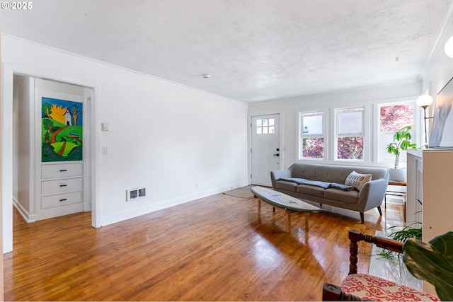 living area featuring baseboards, ornamental molding, wood finished floors, and visible vents