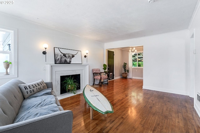 living area featuring crown molding, wood finished floors, a fireplace, baseboards, and a notable chandelier