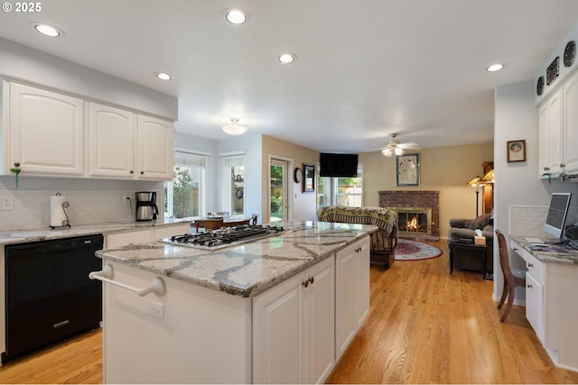kitchen featuring dishwasher, stainless steel gas cooktop, a fireplace, ceiling fan, and a kitchen island